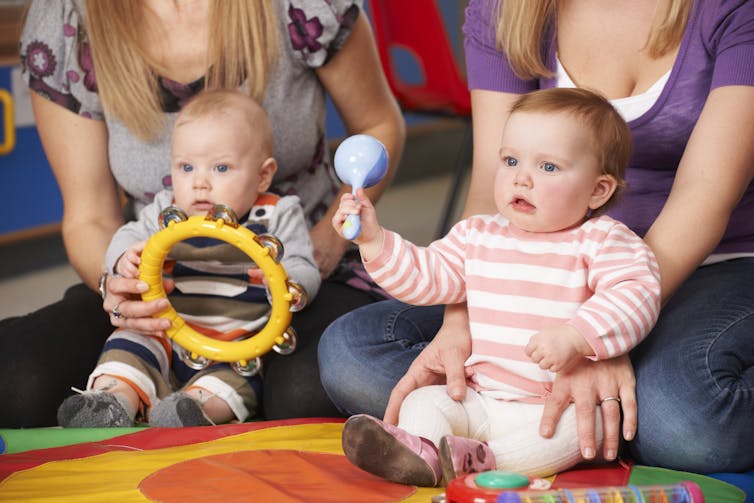 a baby holding a tambourine next to another baby shaking a maraca