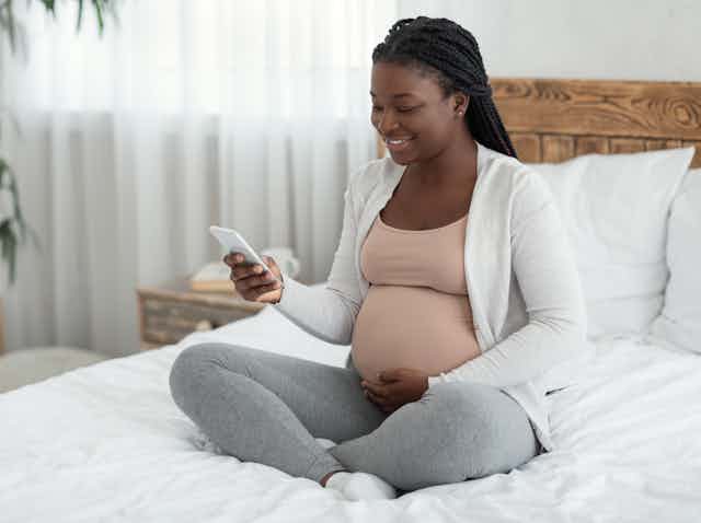 A pregnant woman sitting a bed looking at her mobile phone