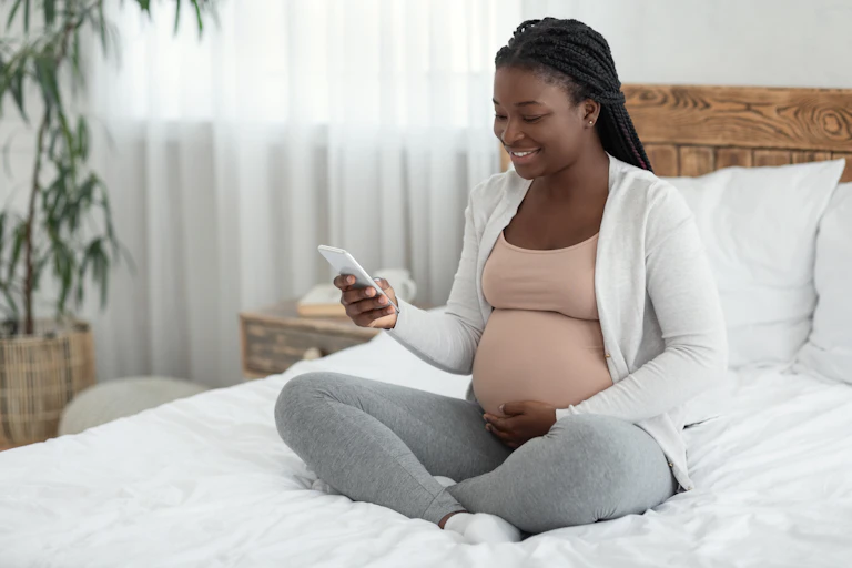 A pregnant woman sitting a bed looking at her mobile phone