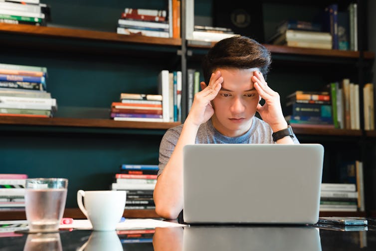 University student struggling to concentrate as he looks at laptop screen