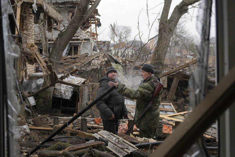 Two men in winter coats survey damage to buildings after an airstrike.
