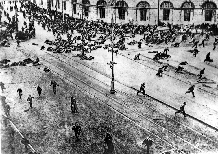 A black-and-white photo shows bodies lying in the streets.