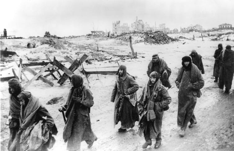 A black and white photo shows German soldiers in tattered uniforms walking in the snow.