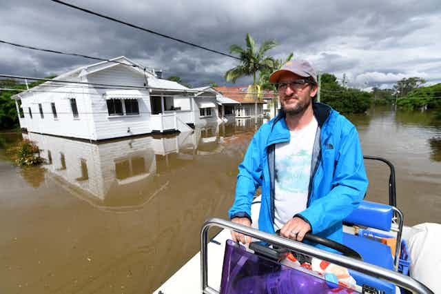man drives boat past flooded houses