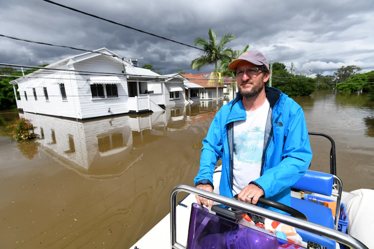 man drives boat past flooded houses