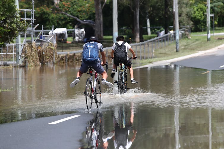 men ride bikes over flooded road