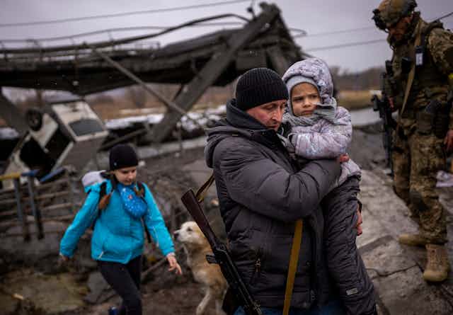Local militiaman Valery, 37, carries a child as he helps a fleeing family across a bridge destroyed by artillery, on the outskirts of Kyiv, Ukraine, Wednesday, March 2. 2022.