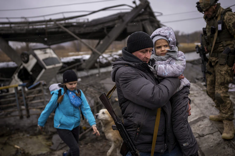 Local militiaman Valery, 37, carries a child as he helps a fleeing family across a bridge destroyed by artillery, on the outskirts of Kyiv, Ukraine, Wednesday, March 2. 2022.
