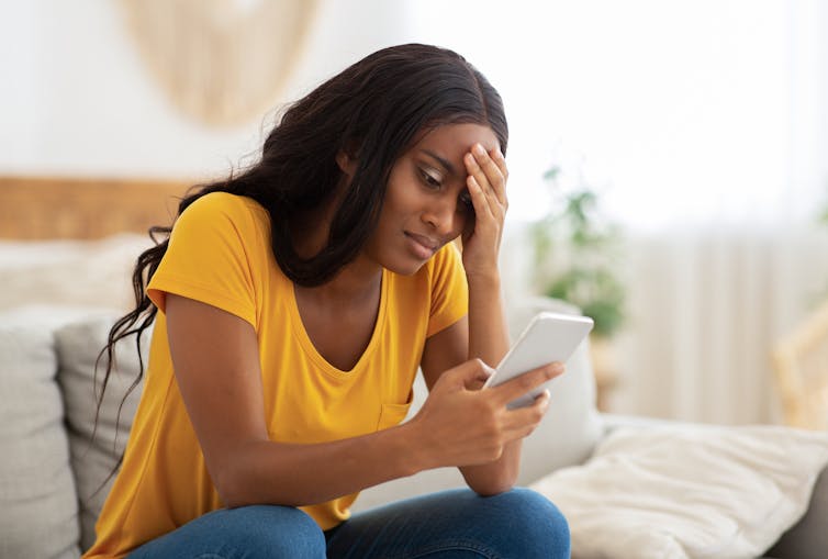 A woman looks at her smartphone, appears unhappy.