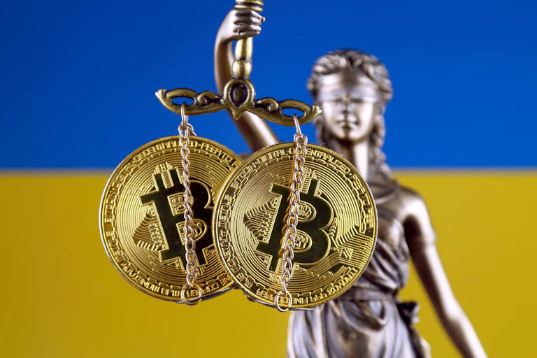 Scales of justice holding bitcoin with Ukraine in the background