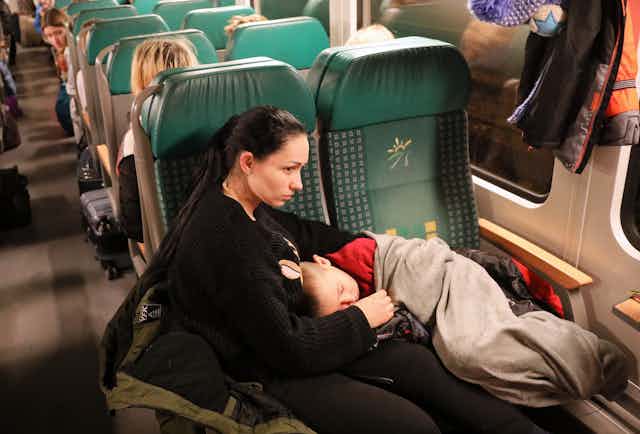 A woman with a sleeping child sitting on a train leaving Ukraine for Poland. 
