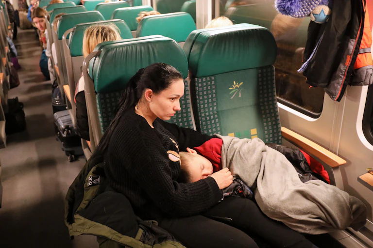 A woman with a sleeping child sitting on a train leaving Ukraine for Poland.
