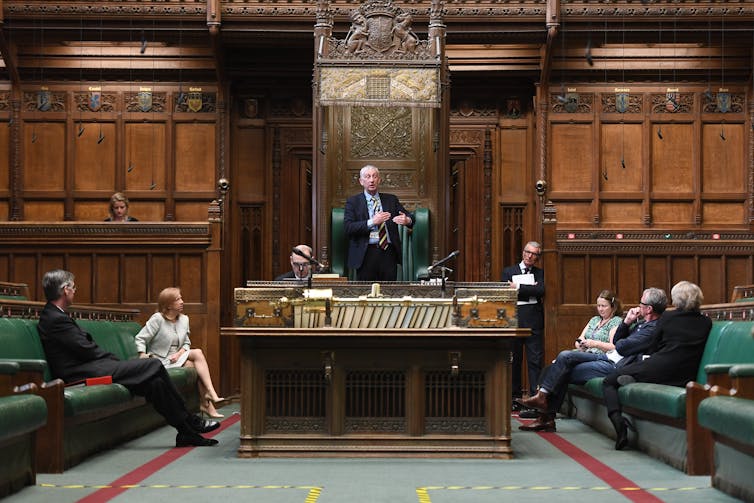 A view inside the House of Commons chamber with the speaker in discussion with front bench MPs and opposition MPs.