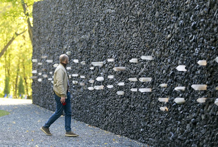 A man walks next to a memorial wall with embedded crystals sommemorating massacre victims at Babyn Yar, Kyiv.