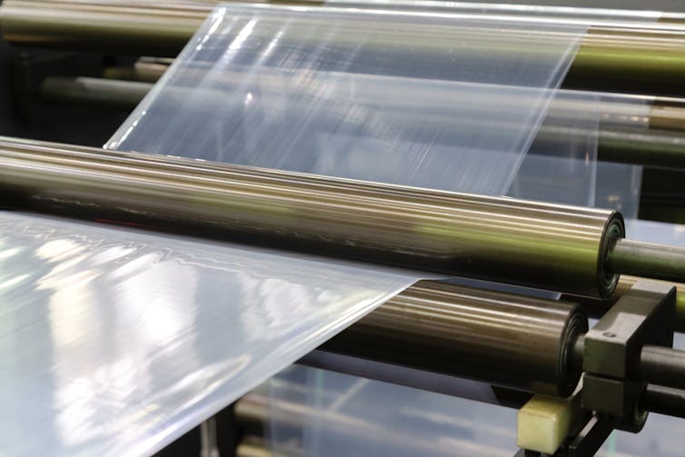 A sheet of plastic packaging stretched on a mechanical roller in a factory.