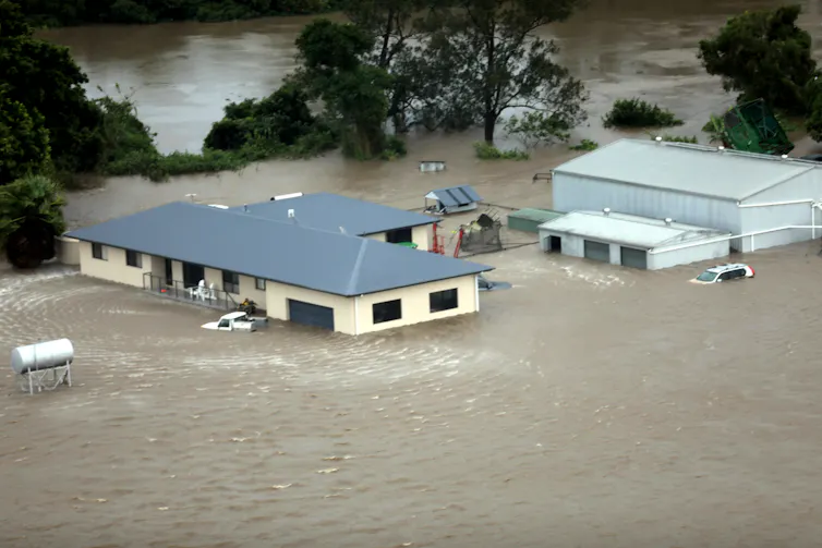 A large house, a shed and two cars are completely submerged in floodwater in regional New South Wales.