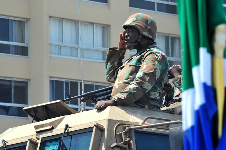 A soldier wearing a military hard hat salutes atop a military vehicle.