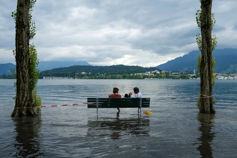 Couple sit on bench in flooded park, nice view