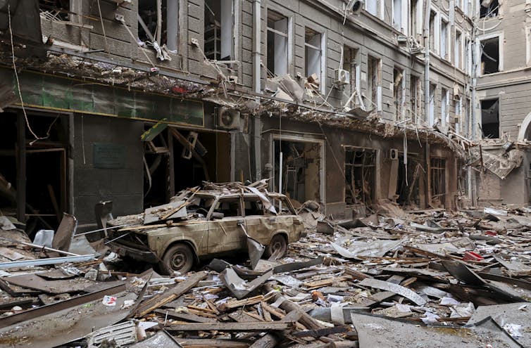 Damaged car sits in front of a bombed-out building.