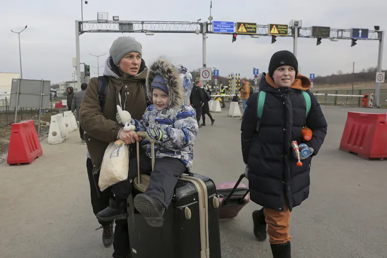 petit garçon assis sur une valise poussée par sa mère, jeune garçon qui marche à côté d’eux
