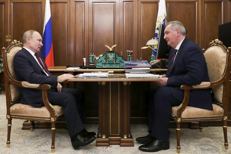 two men in business suits sit at a table, across from each other