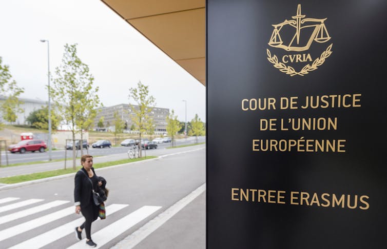 A woman walks by the entrance to a building that says 'Cour de Justice de L'union Europeenne' on the front.