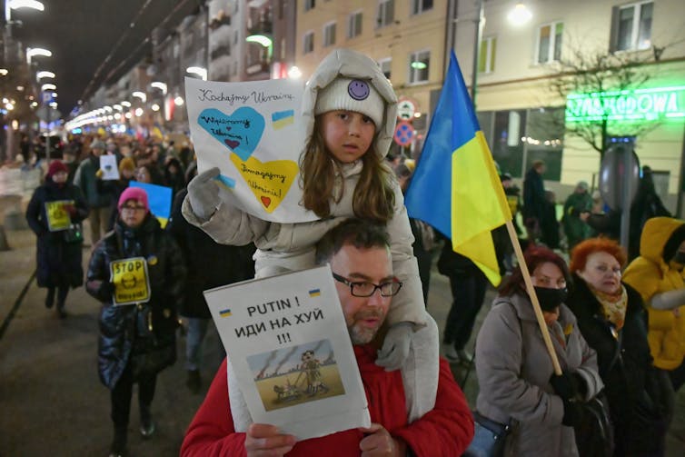Child sits on Dad's shoulders during protest in solidarity with Ukraine in Poland.