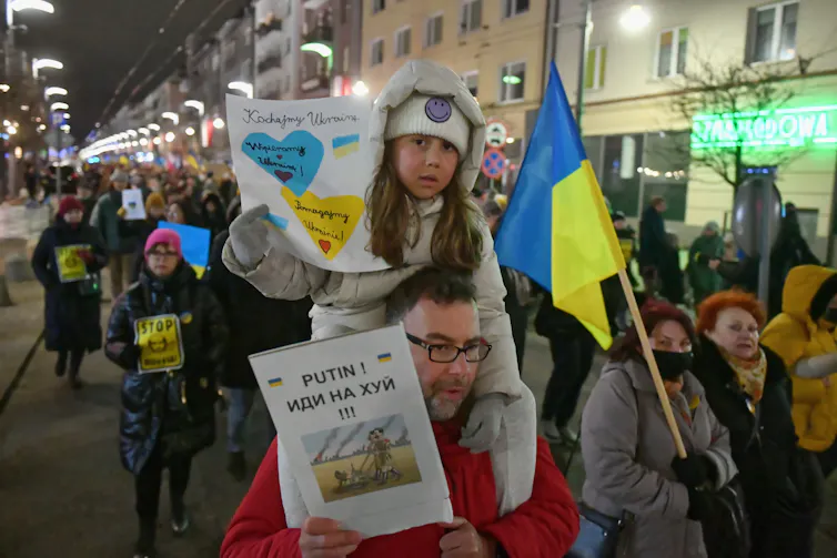 Child sits on Dad's shoulders during protest in solidarity with Ukraine in Poland.