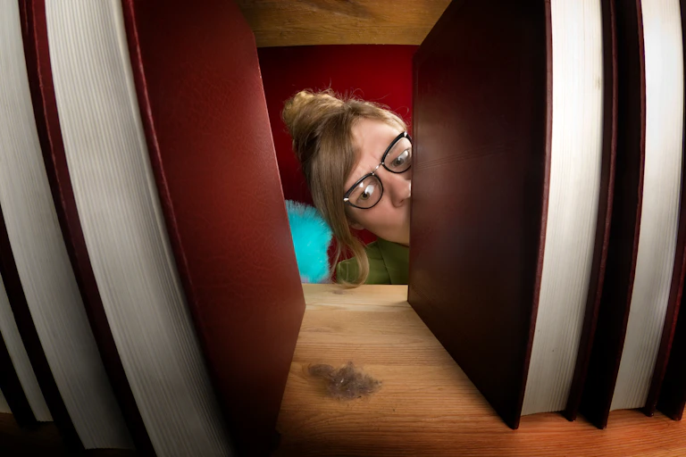 Woman looks through gap in books on shelf