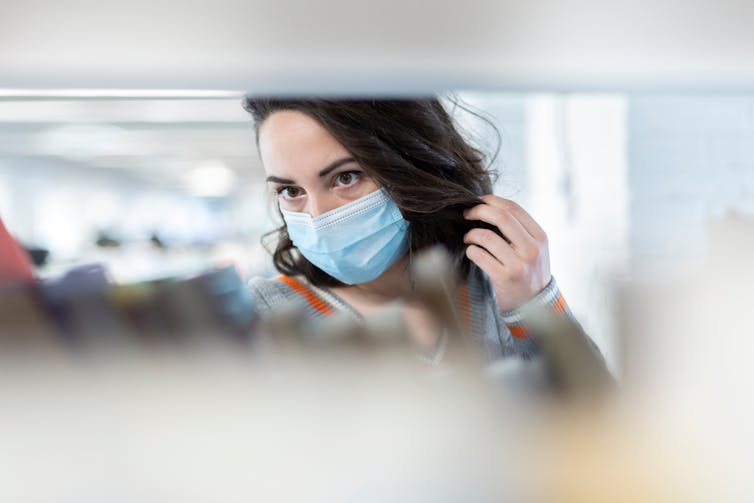 Masked woman looking through journals on a shelf