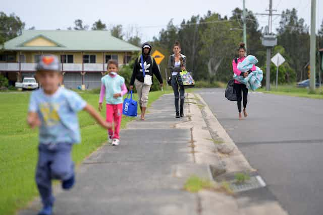 A family is walking down a street with bags of belongings and blankets