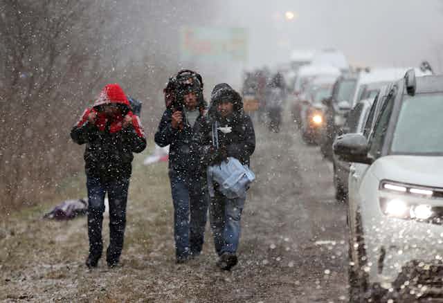 Three people in hoods and carrying backpacks, walking in the rain to the Polish border from Western Ukraine.