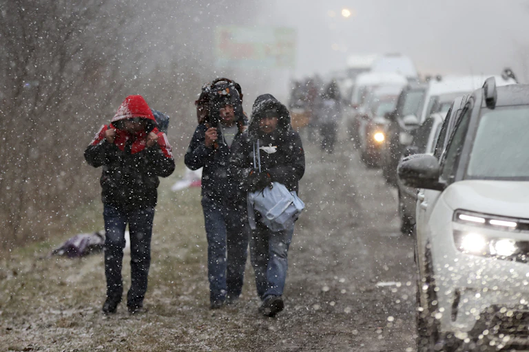 Three people in hoods and carrying backpacks, walking in the rain to the Polish border from Western Ukraine.