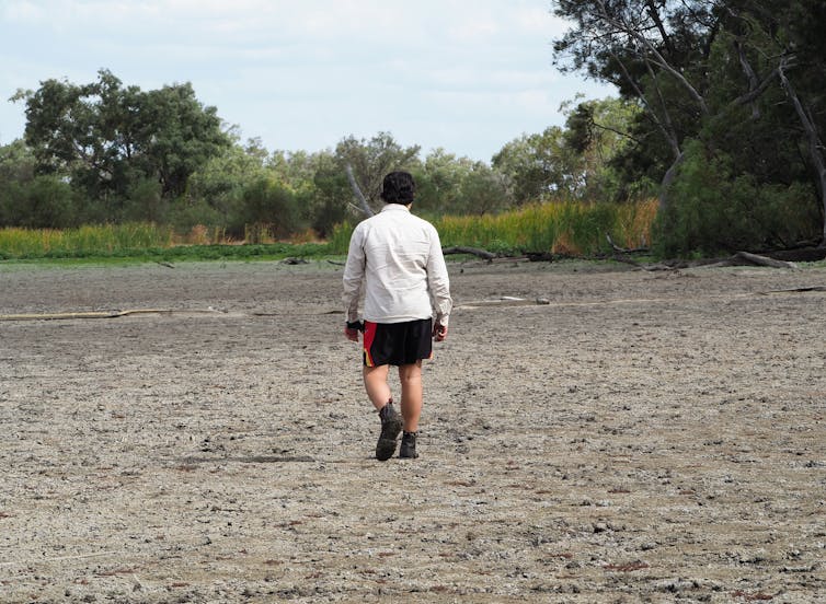 A young person walks across a dried up water hole. They walk with sadness.