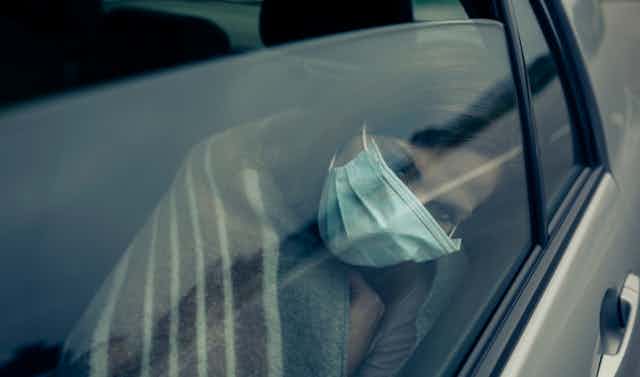 Una mujer abatida con mascarilla apoya su cabeza en el interior del cristal de un vehículo.
