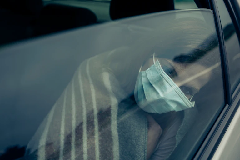 Una mujer abatida con mascarilla apoya su cabeza en el interior del cristal de un vehículo.