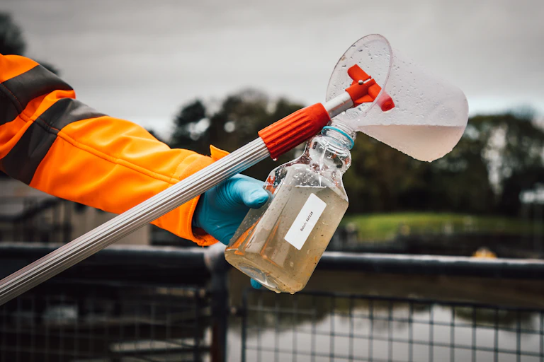 A person collecting a wastewater sample in a bottle