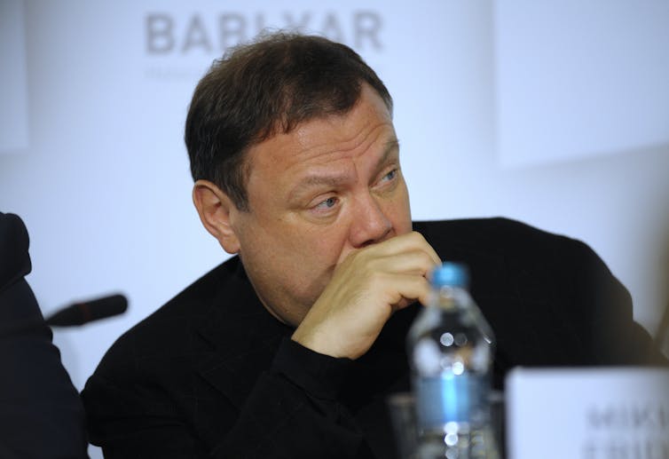 Russian businessman Mikhail Fridman sits with his hand over his mouth and a bottle of water in front of him.
