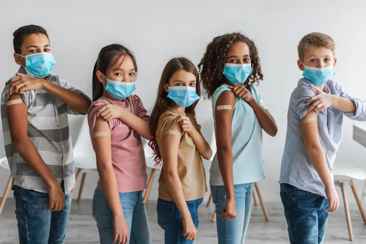 Five children showing plasters on their arms after being vaccinated for COVID