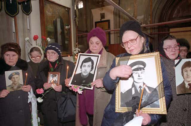 A group of Russian women holding portraits of their sons in army uniforms.