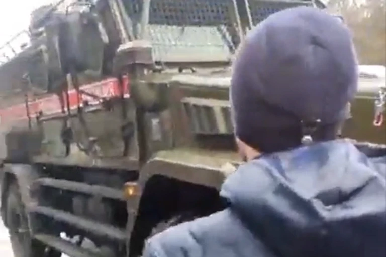 A Ukrainian man wearing a beanie hat stands in front of a Russian truck.