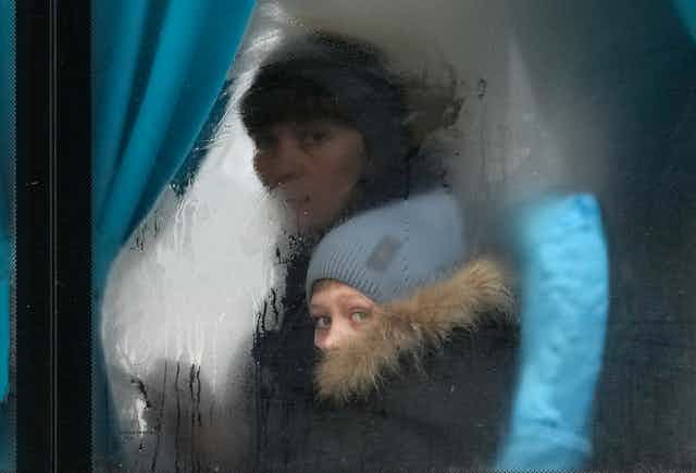 Une femme et un enfant regardent à travers la vitre embuée d'un bus.
