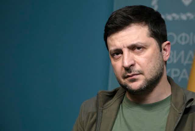 A casually dressed man with dark hair and a scruffy beard looks directly into the camera