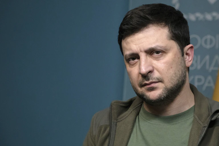 A casually dressed man with dark hair and a scruffy beard looks directly into the camera