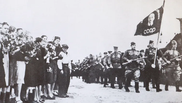 A black and white photograph of crowds greeting solidiers with flags.