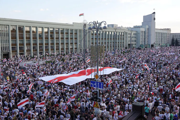 A huge crowd carries flags in front of a large government building in a city centre.