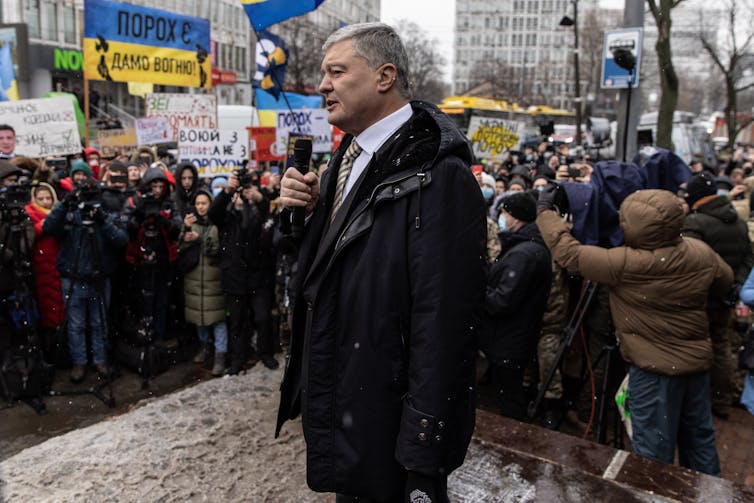 A man dressed in a business suit is holding a microphone in front of a crowd of people.