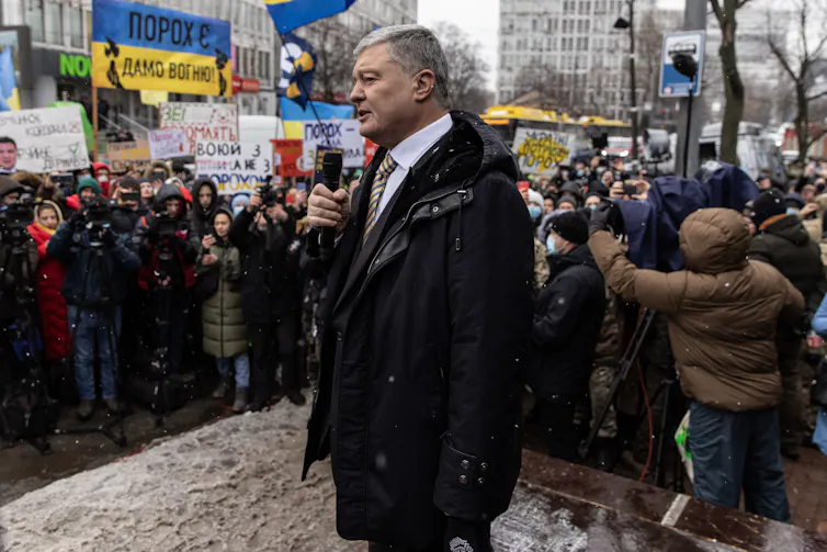 A man dressed in a business suit is holding a microphone in front of a crowd of people.