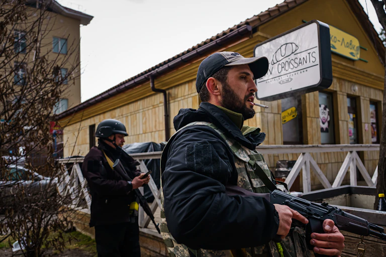 Three men are wearing bullet-proof vests and holding rifles as they stand near a building.