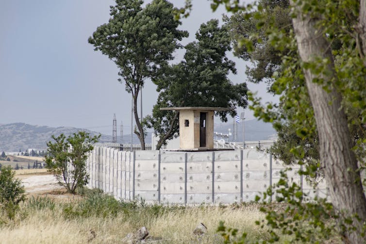 A nearly ten foot high concrete wall is shown with a guard tower.